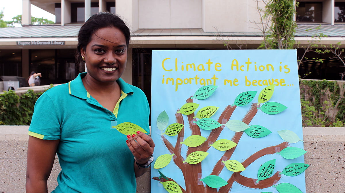 Kavita Nokku poses aside a climate action advocacy poster.